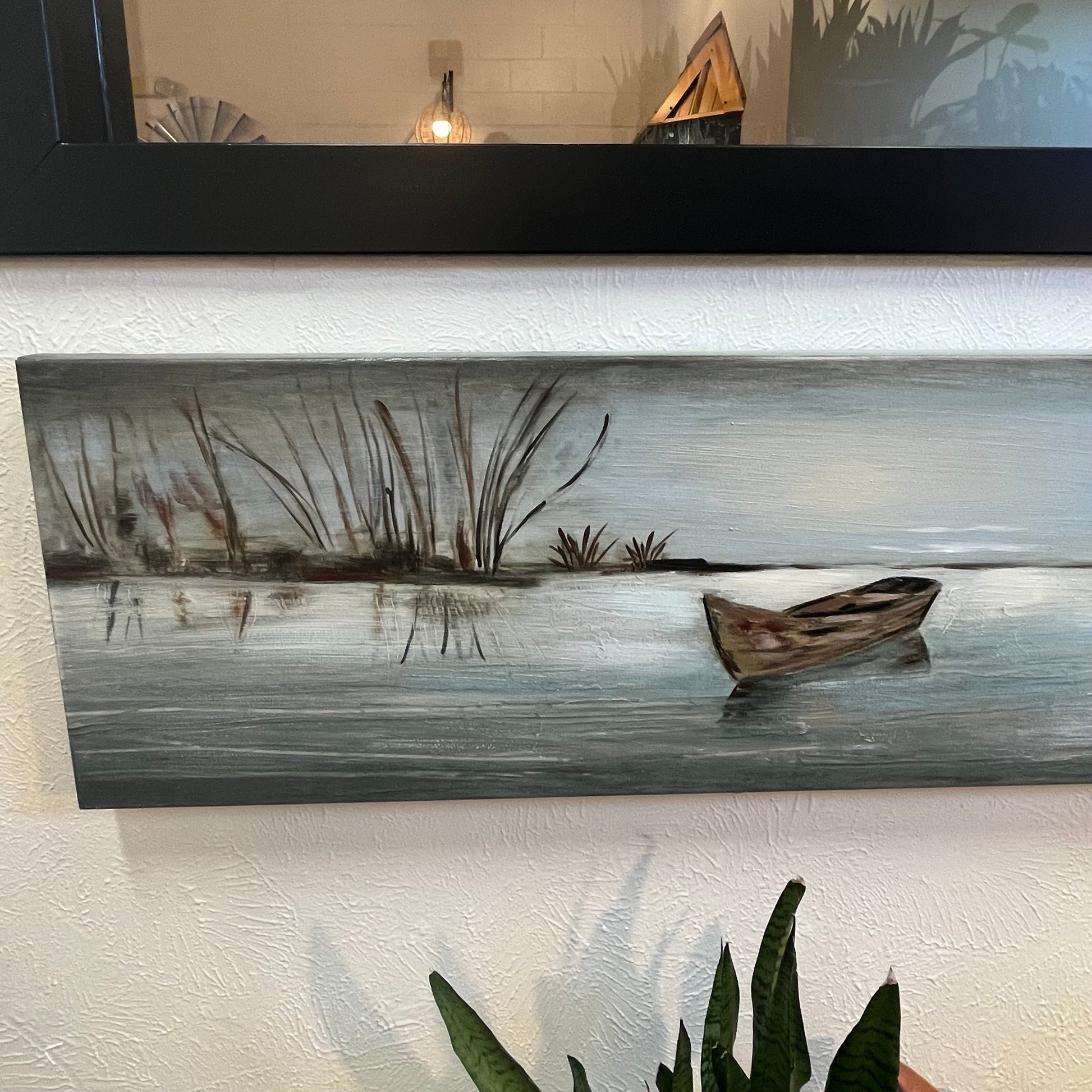 Painting of a boat on water with reeds, displayed on a wall.