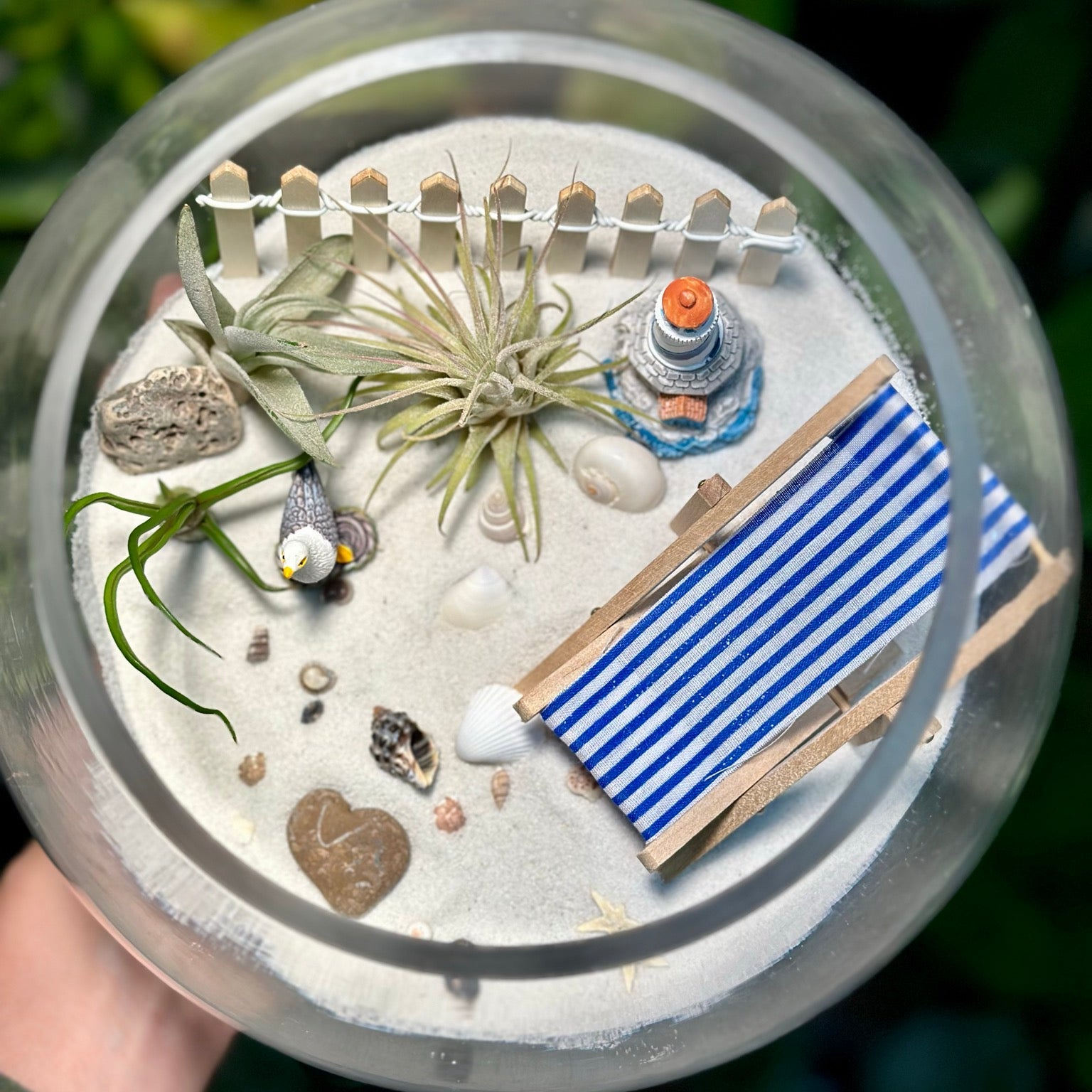 Miniature beach scene in a terrarium with sand, plants, and a striped chair.