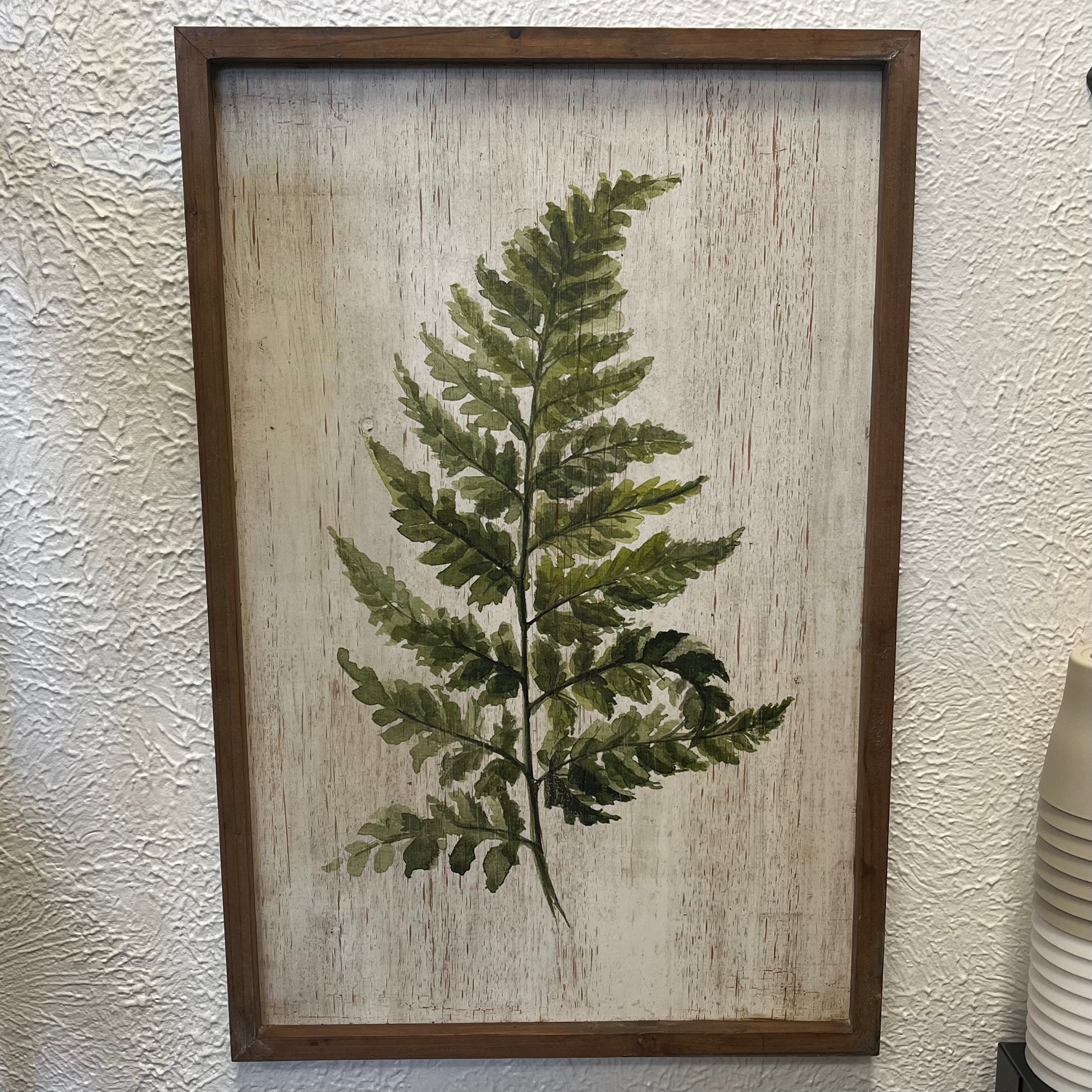 Framed artwork of a green leaf on a textured beige background