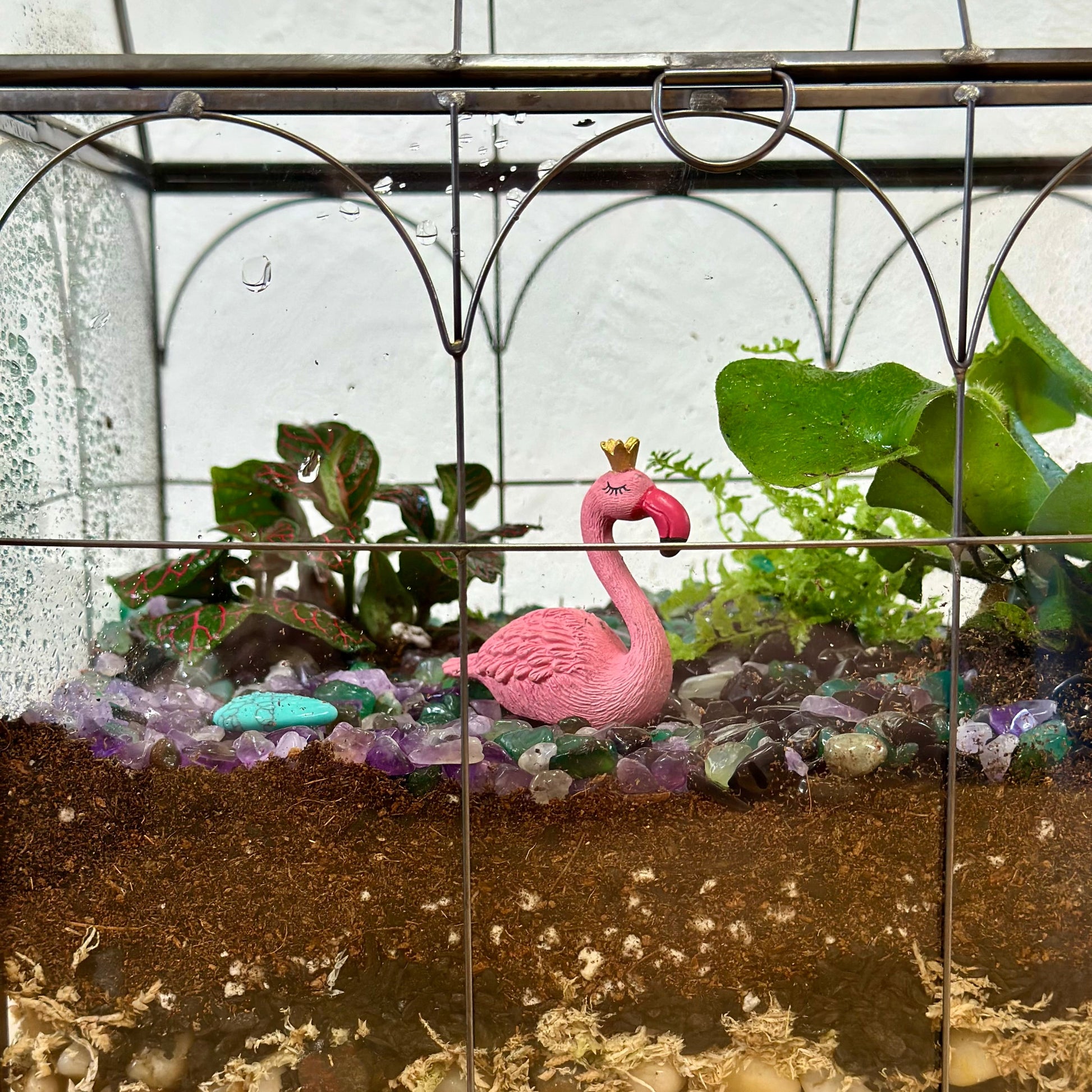 Terrarium with a pink flamingo figurine, plants, and stones inside a glass container.
