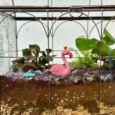 Terrarium with a pink flamingo figurine, plants, and stones inside a glass container.