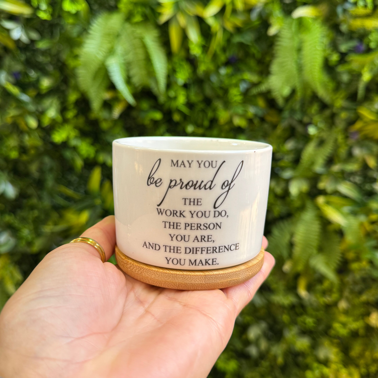 Hand holding a motivational mug with text against a green leafy background