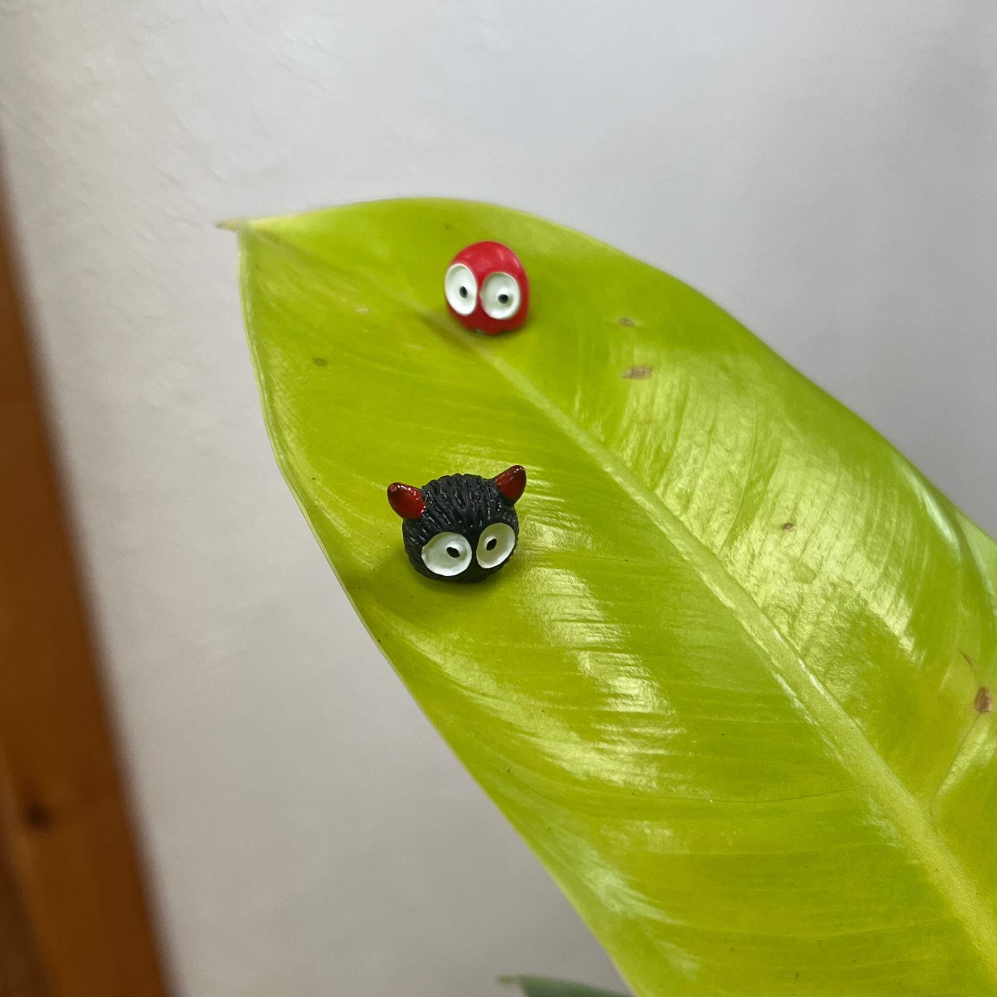 Two small animal-shaped earrings on a green leaf with a plain background