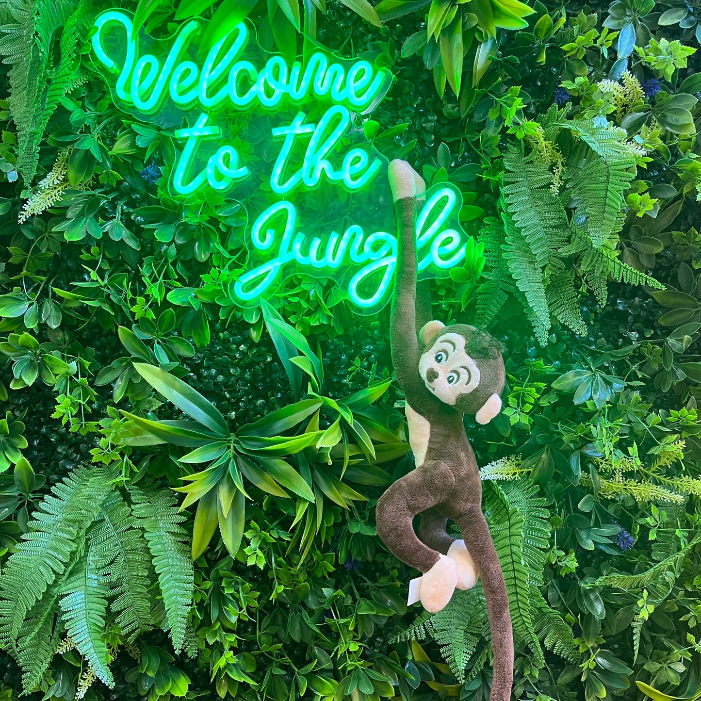 Neon sign saying 'Welcome to the Jungle' with a monkey plush toy on a green leafy background