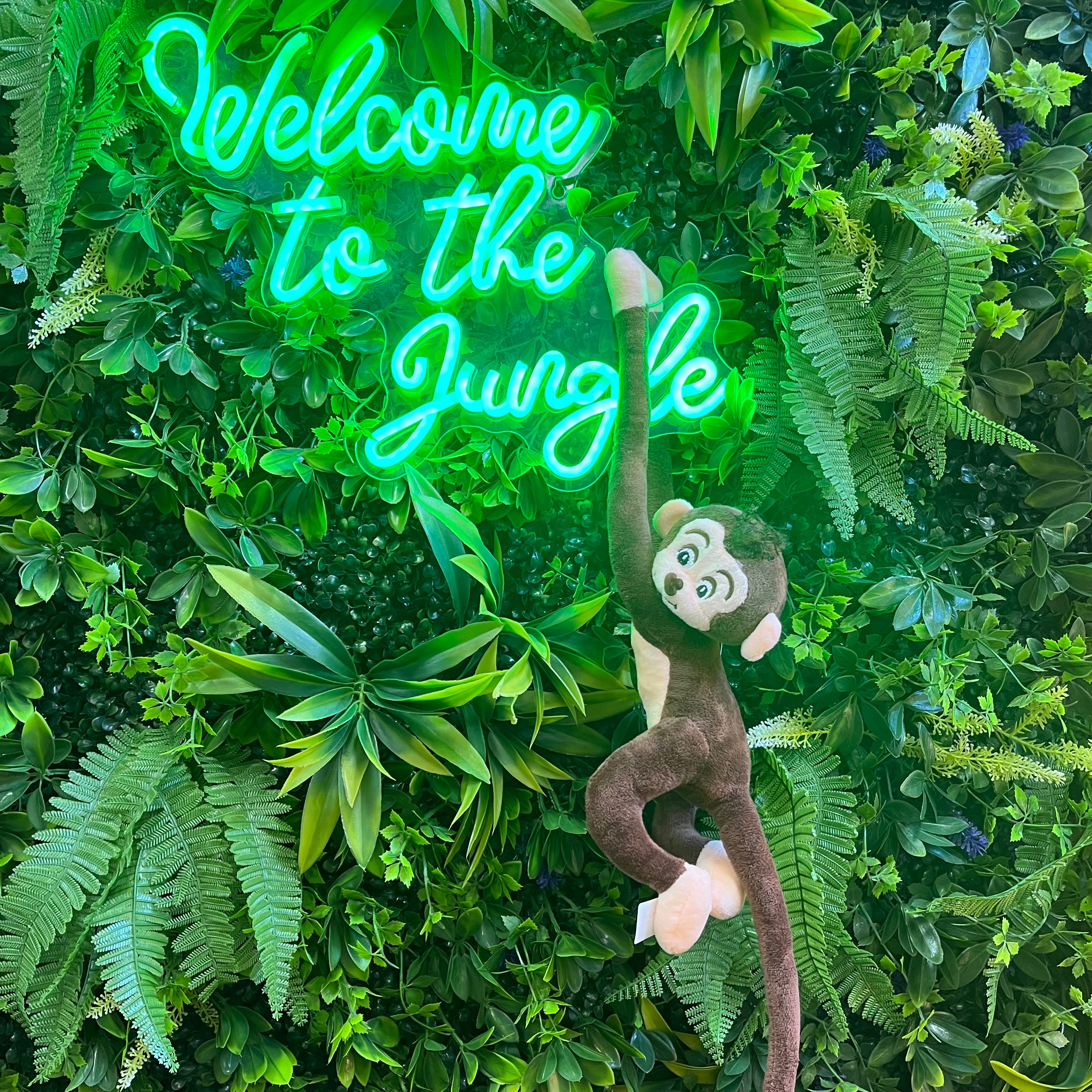 Neon sign saying 'Welcome to the Jungle' with a monkey plush toy on a green leafy background